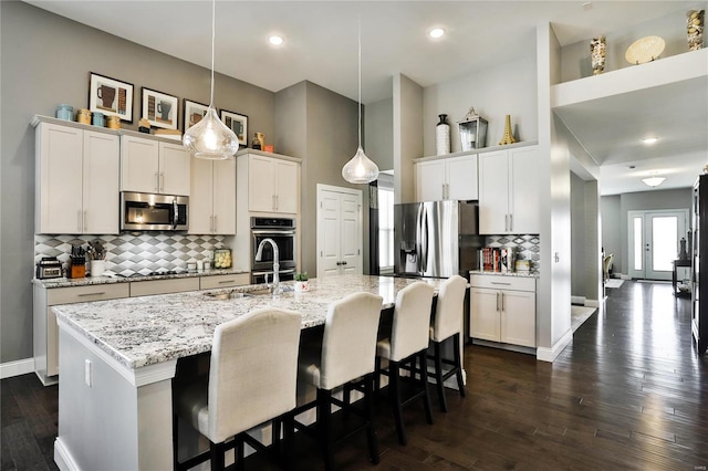 kitchen featuring a center island with sink, hanging light fixtures, stainless steel appliances, dark wood-type flooring, and white cabinetry