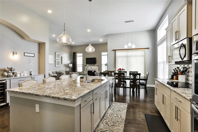 kitchen with dark hardwood / wood-style floors, pendant lighting, appliances with stainless steel finishes, a kitchen island with sink, and light stone counters