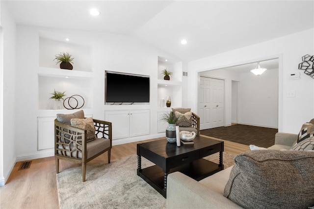 living room with built in features, hardwood / wood-style flooring, and vaulted ceiling