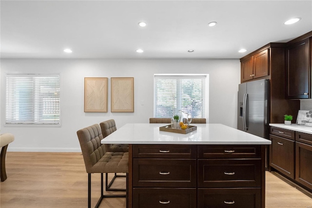 kitchen with stainless steel fridge, light hardwood / wood-style flooring, a kitchen island, and a kitchen breakfast bar