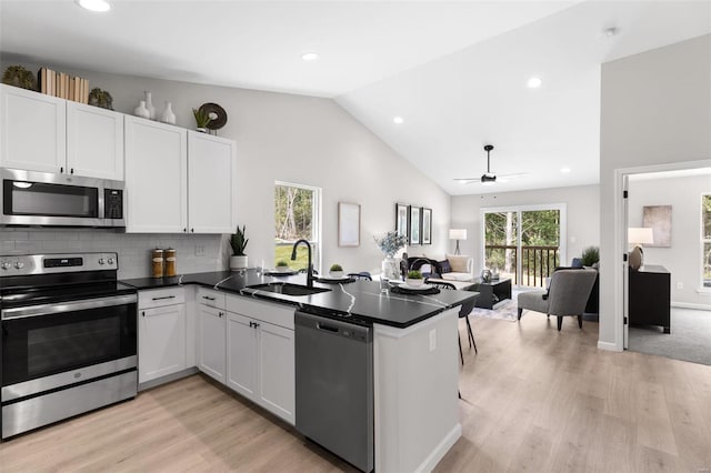 kitchen with stainless steel appliances, dark countertops, open floor plan, a sink, and a peninsula