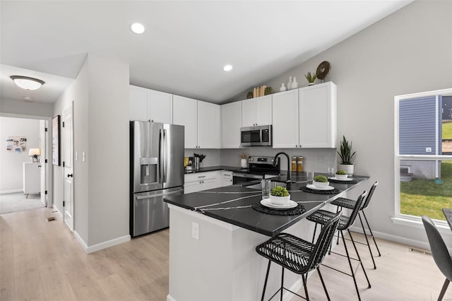 kitchen with light wood-type flooring, a kitchen bar, kitchen peninsula, and stainless steel appliances