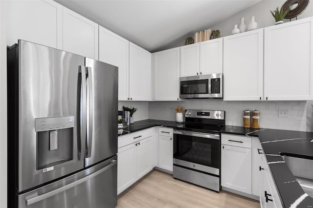 kitchen with vaulted ceiling, appliances with stainless steel finishes, and white cabinets