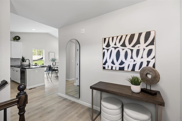 interior space with visible vents, light wood-style floors, vaulted ceiling, a sink, and baseboards