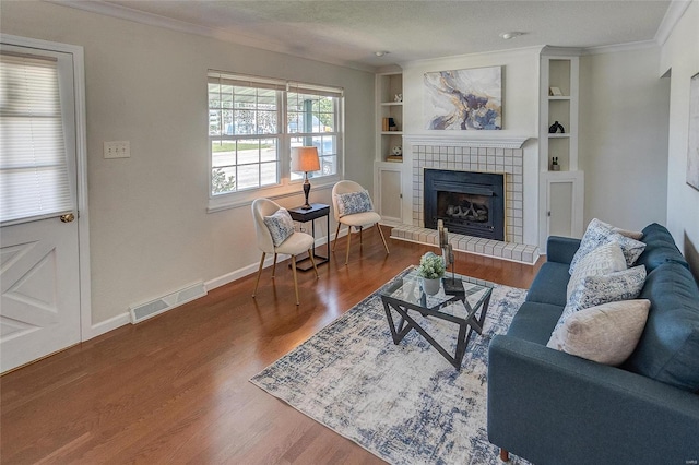 living room featuring a textured ceiling, ornamental molding, a tile fireplace, and hardwood / wood-style flooring