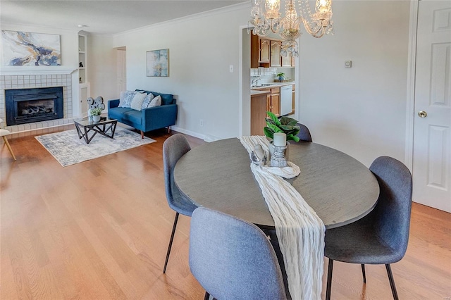 dining space with crown molding, light hardwood / wood-style flooring, a notable chandelier, and a fireplace