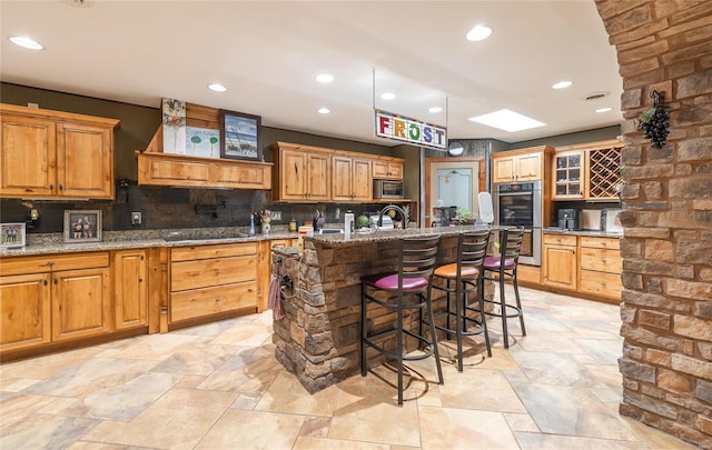 kitchen featuring a breakfast bar area, a center island with sink, stone countertops, premium range hood, and appliances with stainless steel finishes