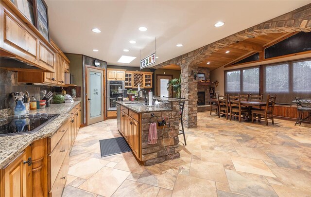 kitchen with stone countertops, sink, lofted ceiling with beams, and a kitchen island with sink