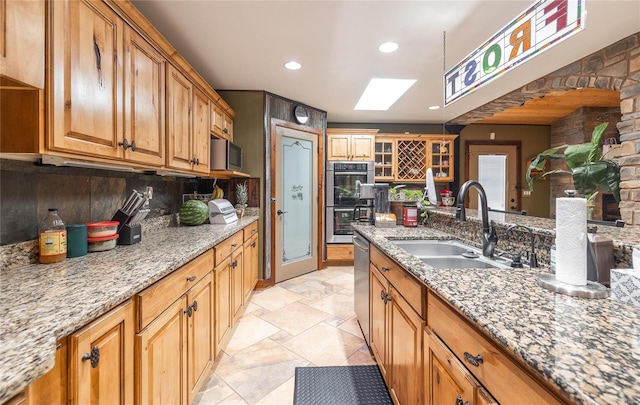 kitchen featuring sink, light stone countertops, appliances with stainless steel finishes, and a skylight