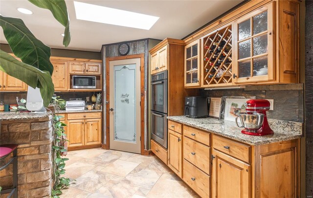 kitchen featuring stainless steel microwave, multiple ovens, backsplash, and light stone countertops