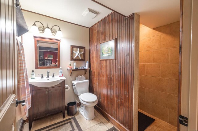 bathroom with tile patterned flooring, wooden walls, toilet, tiled shower, and vanity