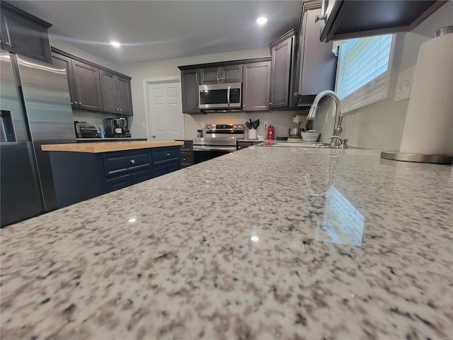 kitchen featuring light stone counters, stainless steel appliances, dark brown cabinets, and sink