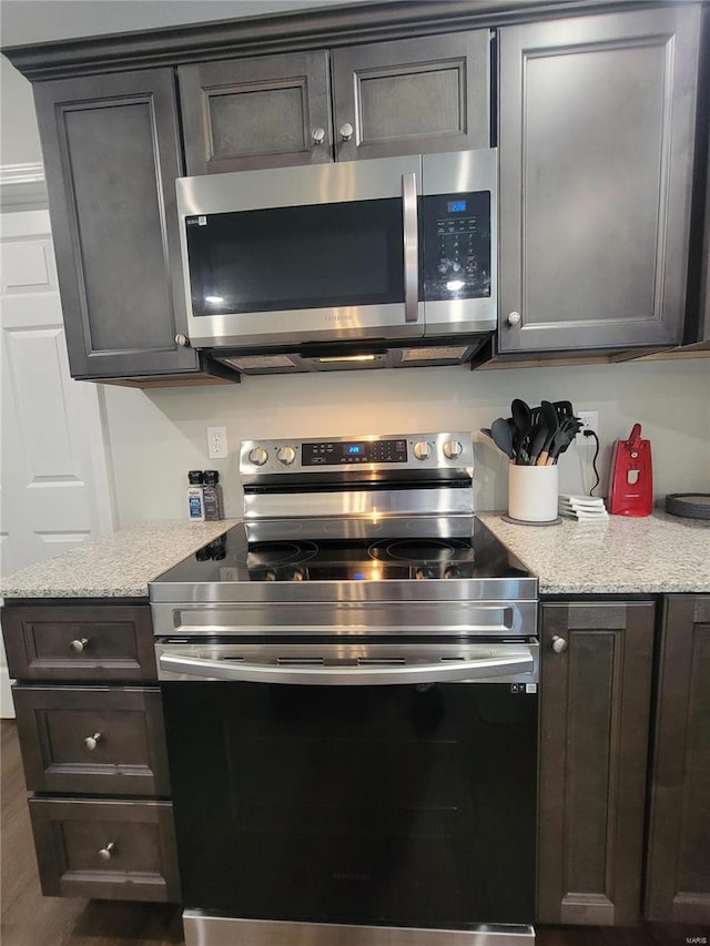 kitchen featuring dark hardwood / wood-style flooring, stainless steel appliances, light stone countertops, and dark brown cabinetry