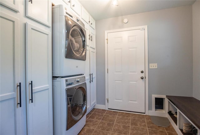 laundry area featuring dark tile patterned flooring, stacked washing maching and dryer, and cabinets