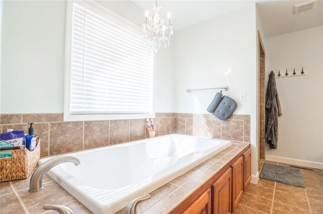 bathroom featuring a notable chandelier, tile patterned floors, and a washtub