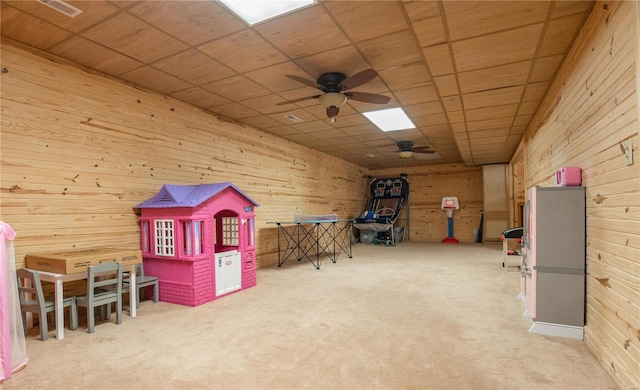 recreation room with a paneled ceiling, wood walls, ceiling fan, and carpet