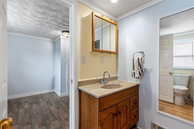 bathroom with a textured ceiling, wood-type flooring, vanity, and toilet