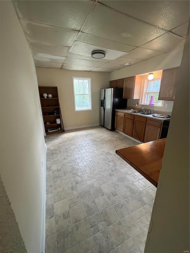 kitchen with a healthy amount of sunlight, a paneled ceiling, stainless steel fridge, and sink