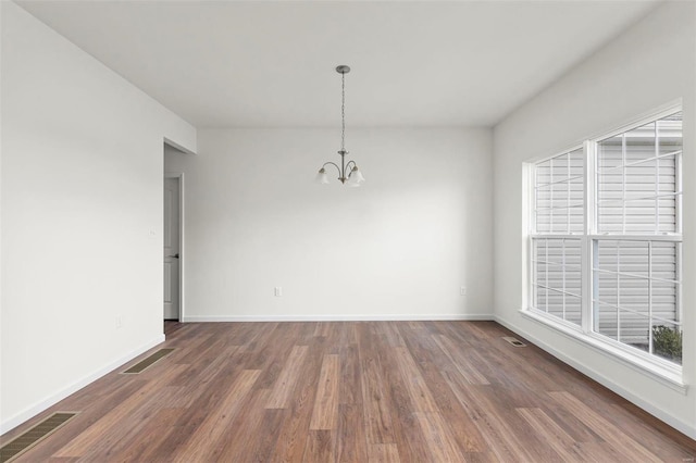 unfurnished room with visible vents, baseboards, an inviting chandelier, and wood finished floors