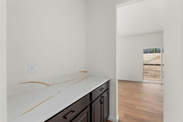 bar with dark brown cabinetry, light stone countertops, and light hardwood / wood-style floors