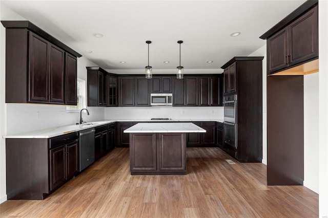 kitchen with decorative light fixtures, appliances with stainless steel finishes, a kitchen island, and light hardwood / wood-style floors