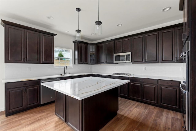 kitchen featuring wood-type flooring, light stone counters, a kitchen island, appliances with stainless steel finishes, and dark brown cabinetry