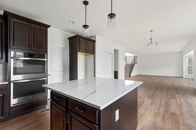 kitchen featuring stainless steel double oven, light hardwood / wood-style flooring, decorative light fixtures, light stone counters, and a kitchen island