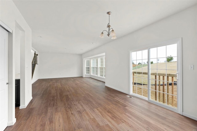 unfurnished living room with a healthy amount of sunlight, an inviting chandelier, and hardwood / wood-style floors