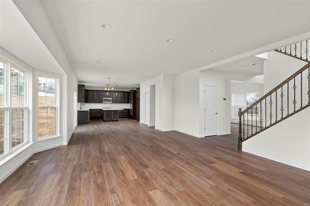 unfurnished living room with stairway, baseboards, recessed lighting, a sink, and dark wood-type flooring