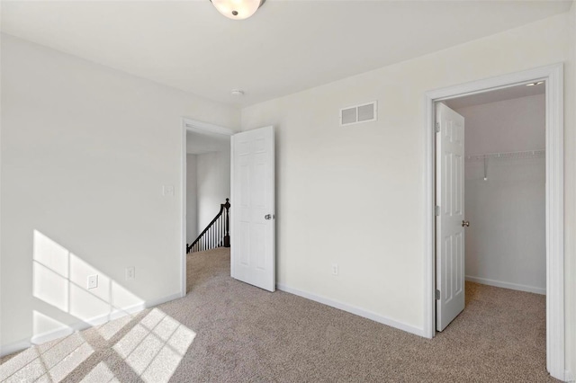 unfurnished bedroom with a spacious closet, carpet, visible vents, and baseboards