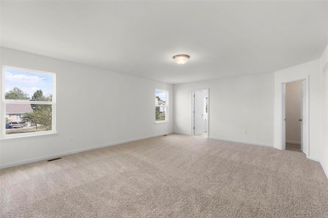 spare room with plenty of natural light, light colored carpet, visible vents, and baseboards