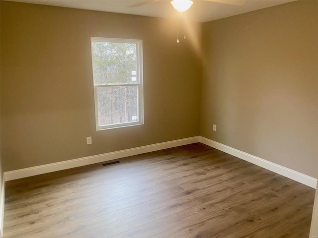 empty room featuring a ceiling fan, visible vents, baseboards, and wood finished floors