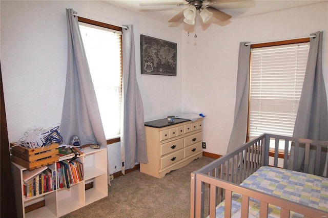 bedroom with multiple windows, a crib, ceiling fan, and carpet floors