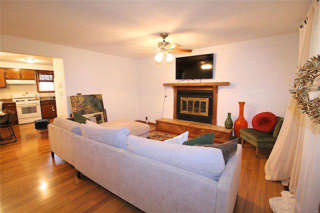 living room with a tiled fireplace, ceiling fan, and light hardwood / wood-style floors