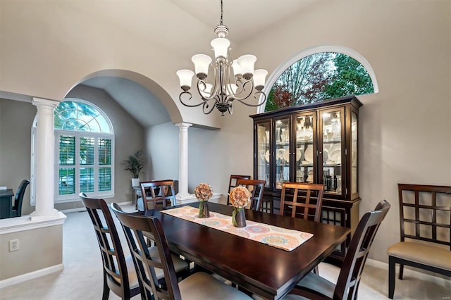 carpeted dining room featuring ornate columns, vaulted ceiling, and an inviting chandelier