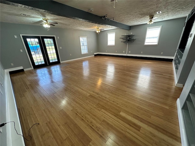 unfurnished living room with a textured ceiling, beamed ceiling, ceiling fan, and hardwood / wood-style flooring