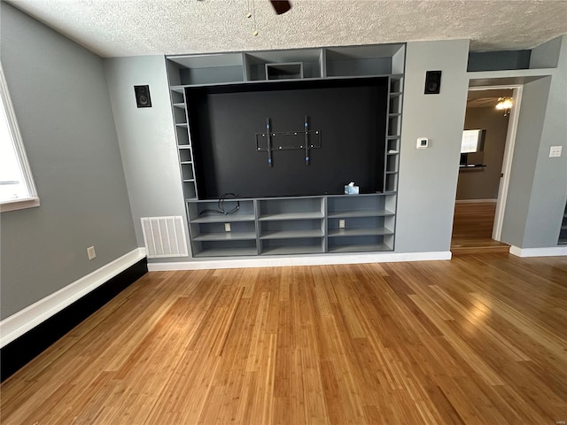 unfurnished living room with a textured ceiling, wood-type flooring, and ceiling fan