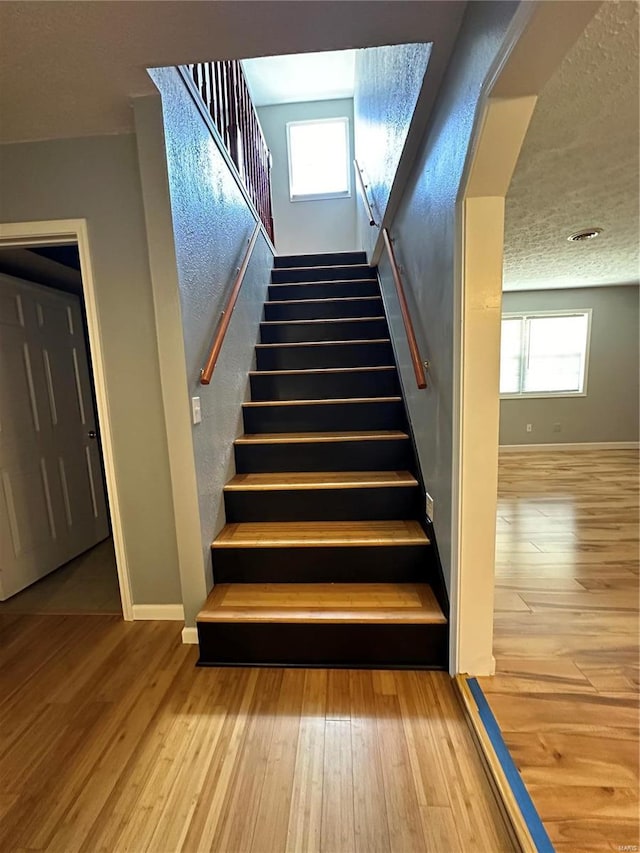 stairway with wood-type flooring and a textured ceiling