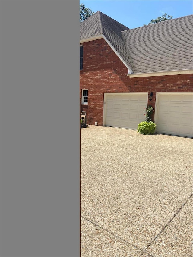 view of home's exterior with a garage, brick siding, driveway, and a shingled roof