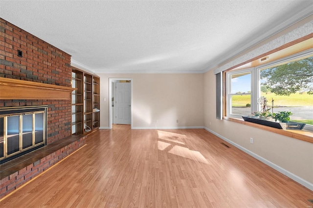 unfurnished living room with a textured ceiling, light hardwood / wood-style floors, ornamental molding, and a brick fireplace