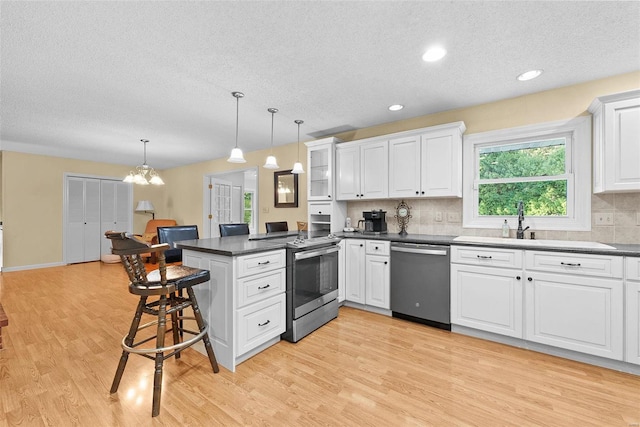 kitchen with appliances with stainless steel finishes, kitchen peninsula, pendant lighting, and white cabinets