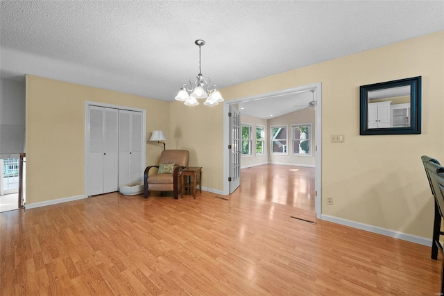 interior space featuring ceiling fan with notable chandelier, lofted ceiling, light hardwood / wood-style floors, and a textured ceiling