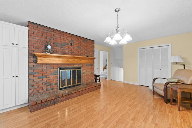 living room featuring a textured ceiling, light hardwood / wood-style floors, an inviting chandelier, and a brick fireplace