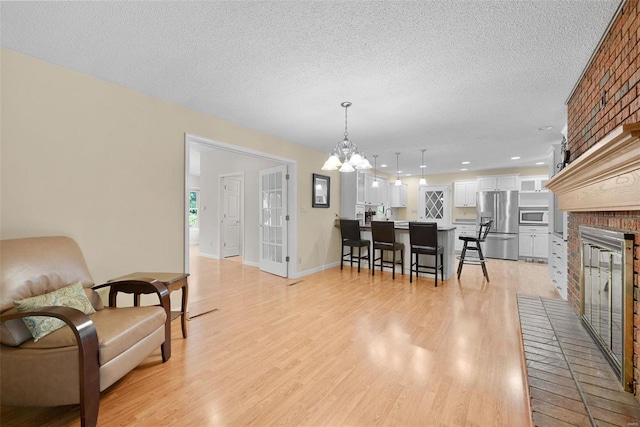 dining area with a notable chandelier, a brick fireplace, light hardwood / wood-style floors, and a textured ceiling