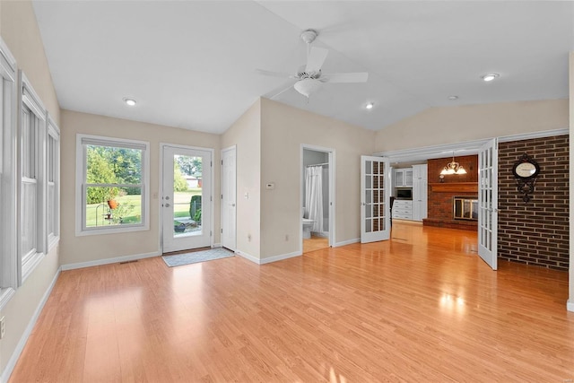 unfurnished living room featuring light wood-type flooring, ceiling fan with notable chandelier, a fireplace, and vaulted ceiling