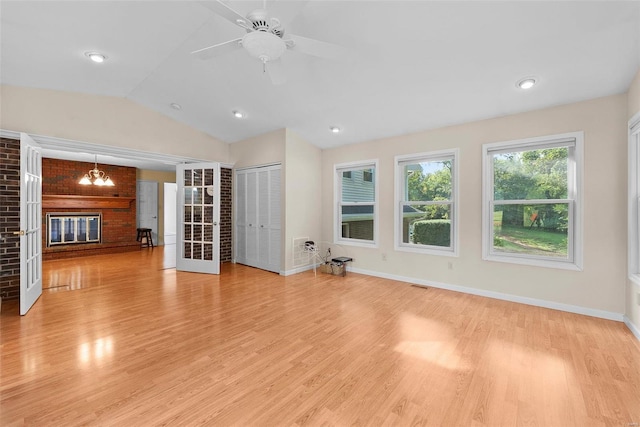 unfurnished living room with ceiling fan with notable chandelier, a brick fireplace, vaulted ceiling, and light hardwood / wood-style floors