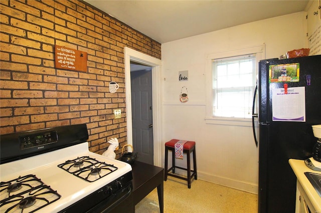 kitchen featuring brick wall, gas range gas stove, and black fridge