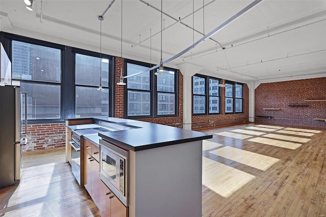 kitchen featuring appliances with stainless steel finishes, light hardwood / wood-style floors, a kitchen island with sink, and brick wall