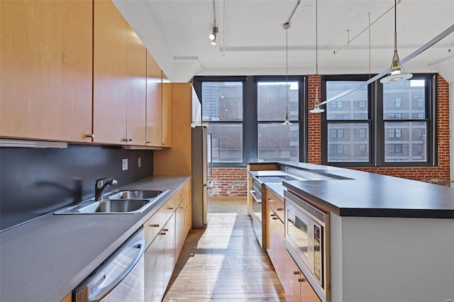 kitchen with light wood-type flooring, appliances with stainless steel finishes, brick wall, and sink