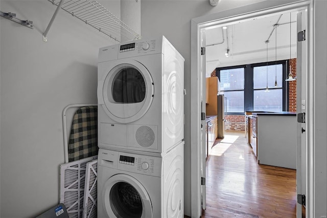 washroom with stacked washer / drying machine and hardwood / wood-style flooring